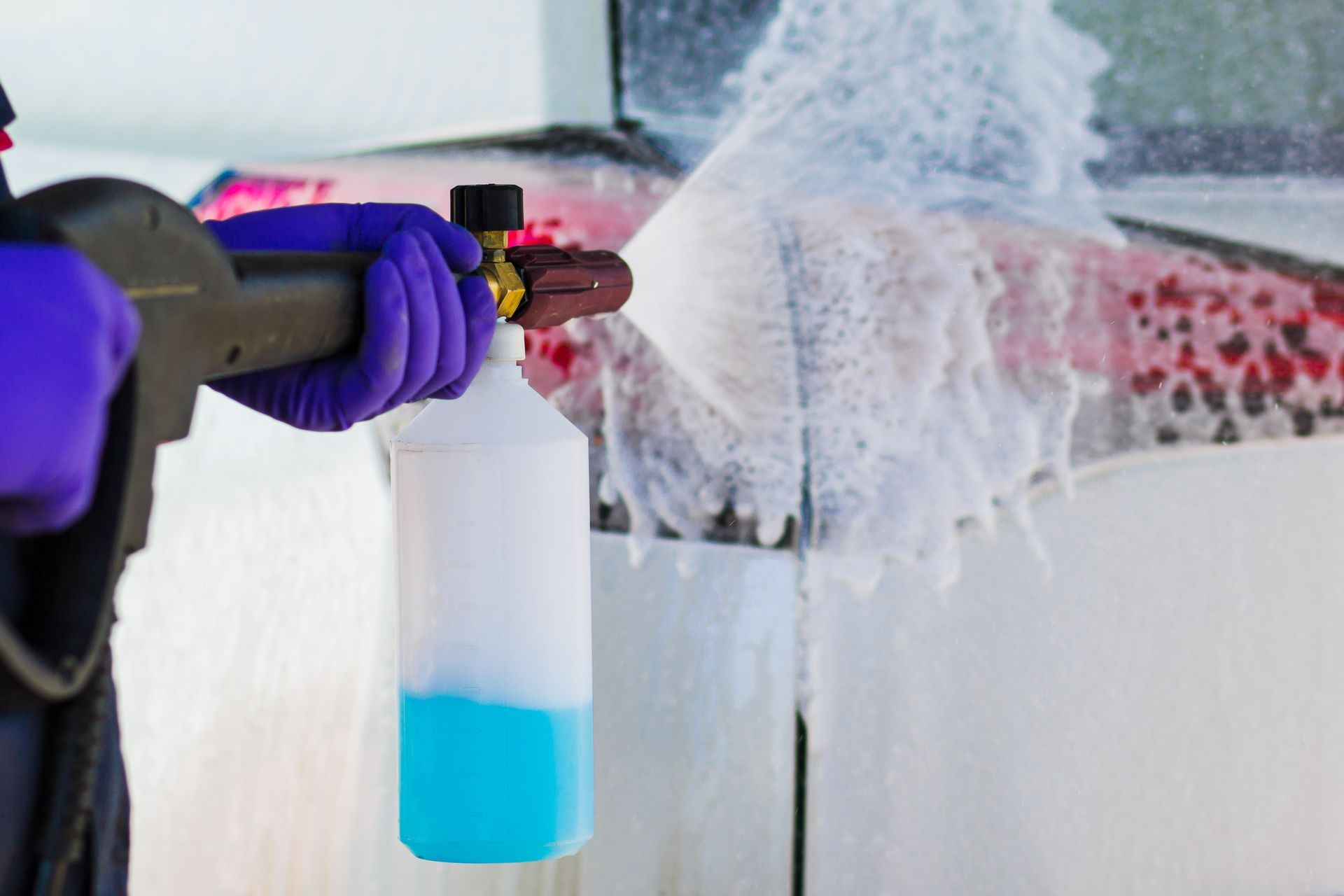 Male hands in blue gloves holding apparatus for spraying foam. Car wash.